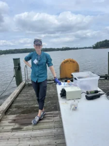 A woman stands on a dock smiling at the camera